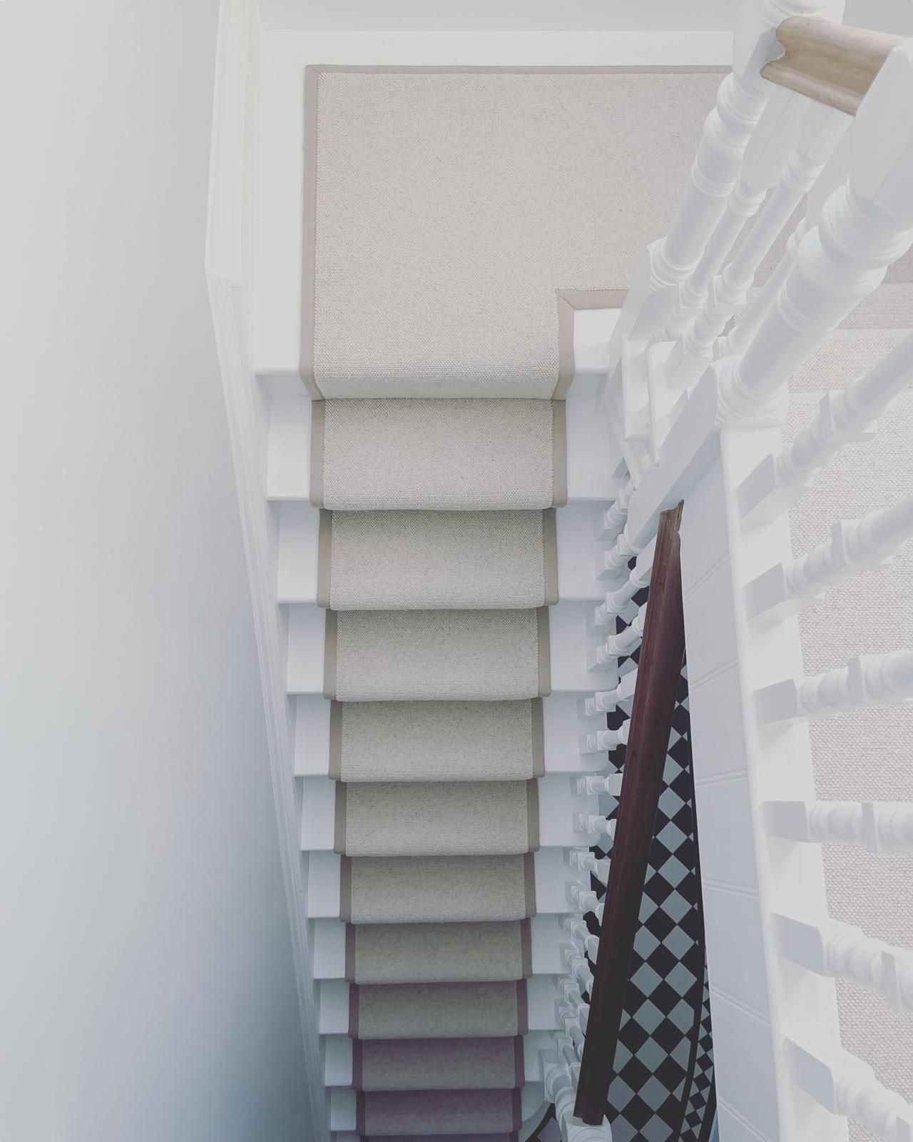 Light neutral stair runner on a white Victorian hallway staircase with checkered floor tiles.
